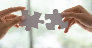 Two hands connecting puzzle pieces symbolizing the strategic fit of digital marketing and client acquisition in lead generation for financial advisors.