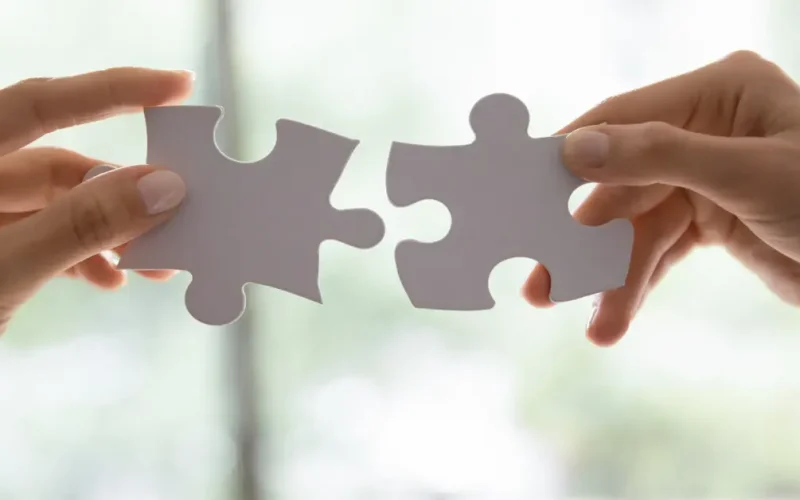 Two hands connecting puzzle pieces symbolizing the strategic fit of digital marketing and client acquisition in lead generation for financial advisors.